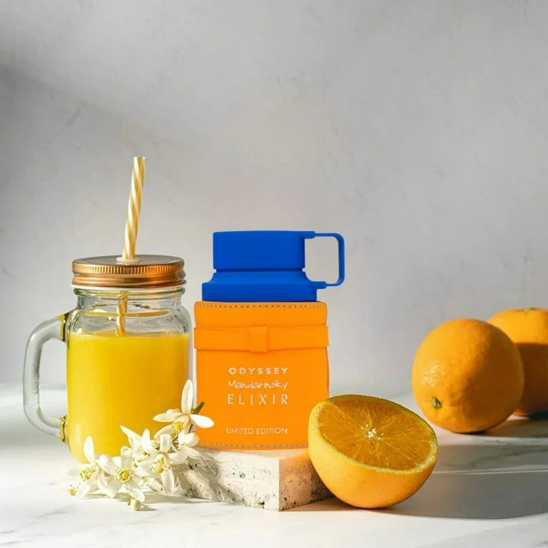 Orange juice in a mason jar with a straw, orange slices, and an orange container labeled 'Odyssey' on a light gray background.