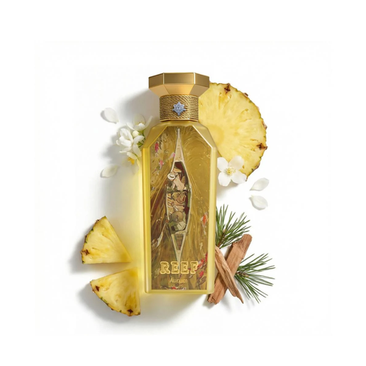 A rectangular perfume bottle with a gold cap, featuring a vintage-style illustration of a woman in a boat and the brand name 'REEF' on the front. The bottle is styled with pineapple slices, white flowers, cinnamon sticks, and pine needles on a clean white background.