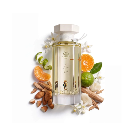 A clear rectangular bottle of sea oil fragrance with a white cap, surrounded by citrus slices, green limes, cinnamon sticks, almonds, and white flowers on a white background. The bottle label shows the brand name REEF.